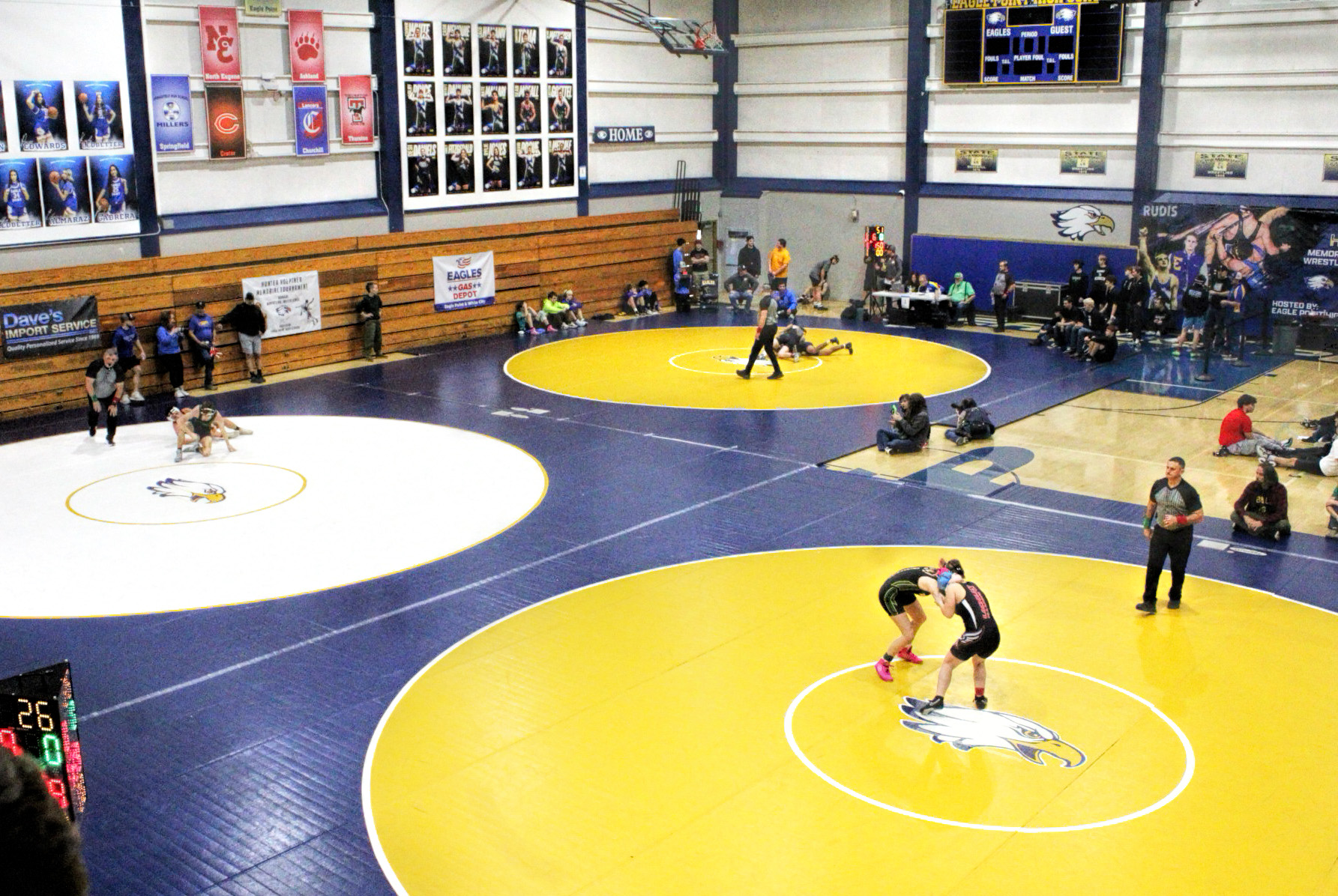 High, wide shot of a high school wrestling tournament with several matches going on at once.