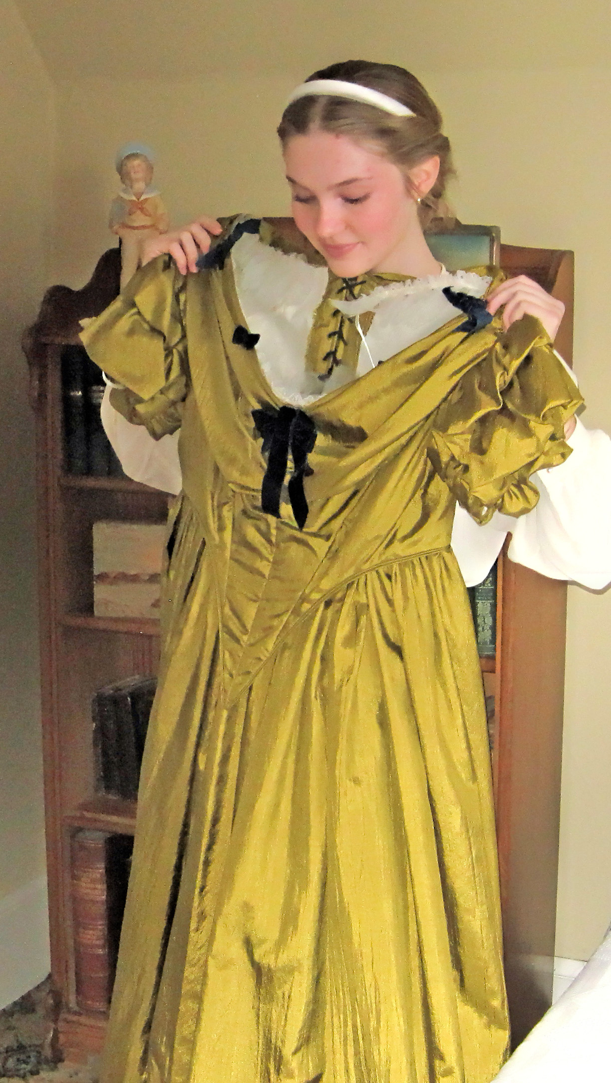 Photo of a young girl in historic costume holding a gold silken gown up in front of her as she looks in a mirror.