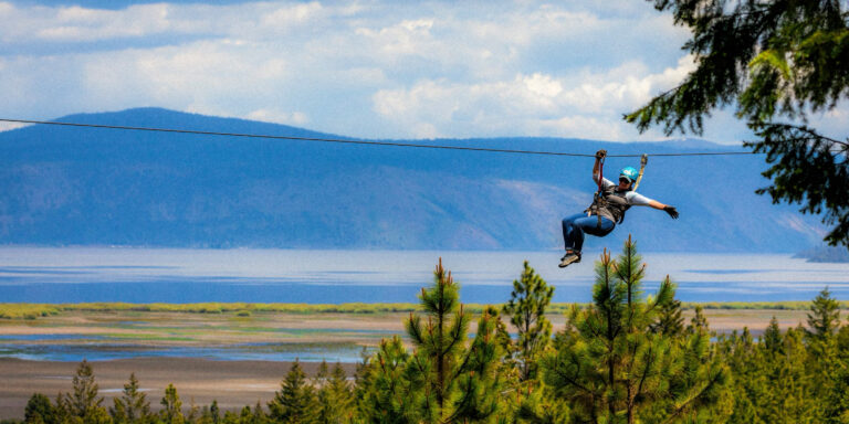 photo at eye level of a person ziplining with Klamath Lake in the background.