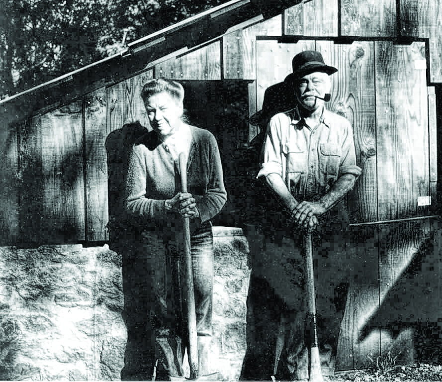 black and white photo of a couple standing in front of a wooden cabin.