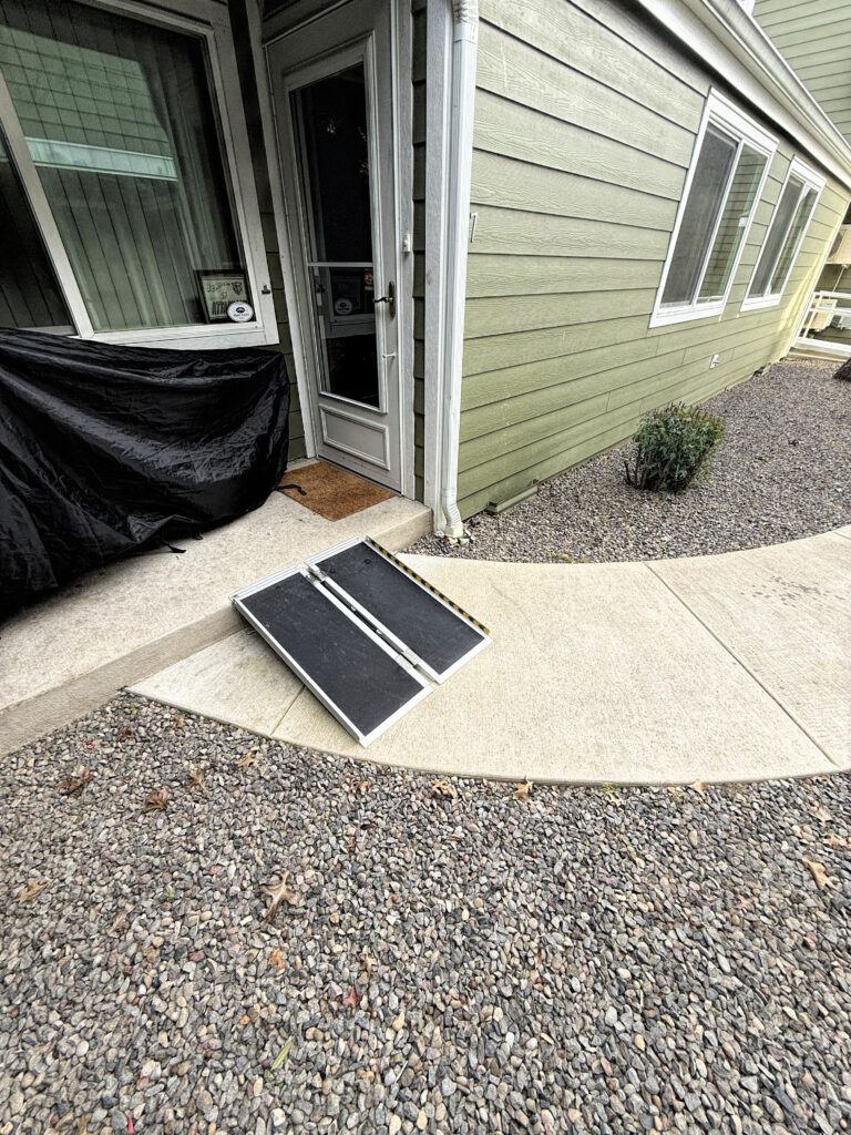 photo of a wheelchair ramp from a porch to a curved walkway so the end of the ramp is almost in the surrounding gravel.