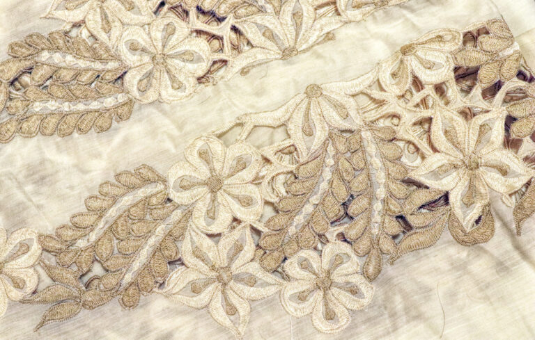 close up photo of intricate embroidery on off white silk material.