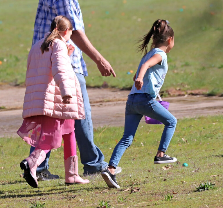 Photo of two girls next to an adult male, the girls are running to gather eggs in an egg hunt.