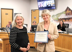 photo of two women smiling at the camera. the one on the right is holding an award certificate.