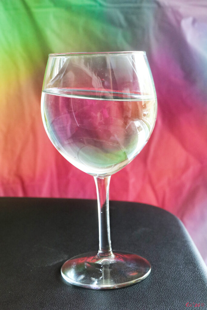 photo of a wine glass with water in it in front of a rainbow colored cloth.