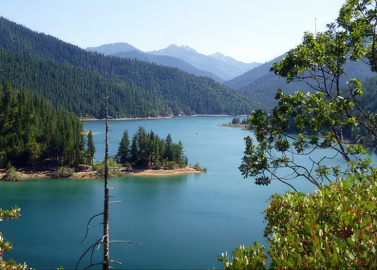 a photo of a reservoir surrounded by conifers and mountains.