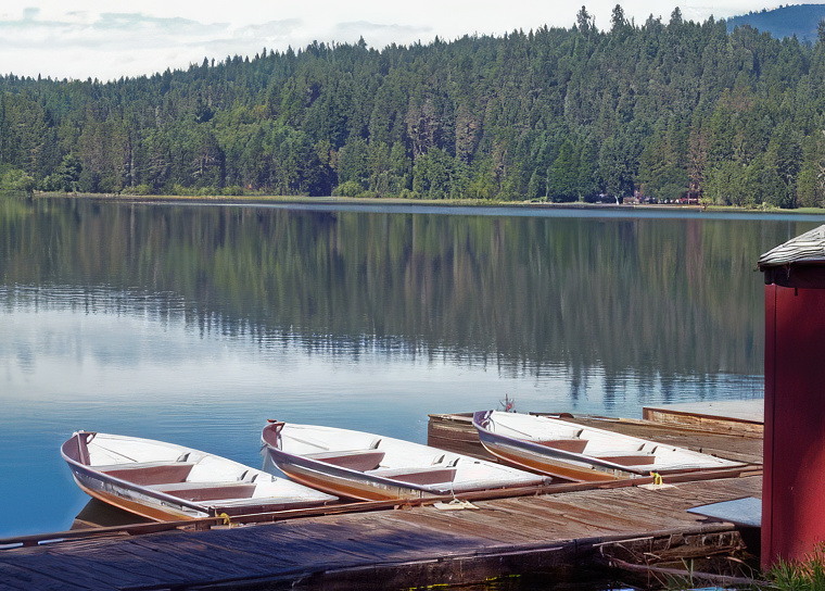 photo of a mountain lake with a dock in the foreground. three small fishing boats are tied ot the dock.