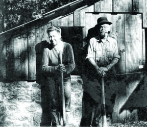black and white photo of a couple in the late 60s standing in front of a wooden structure.