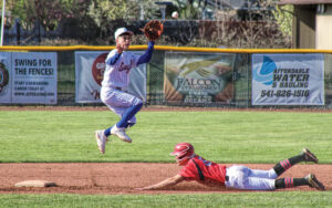photo of a high school baseball game. one player is sliding into a base, the on base player is in mid air about to catch the ball.