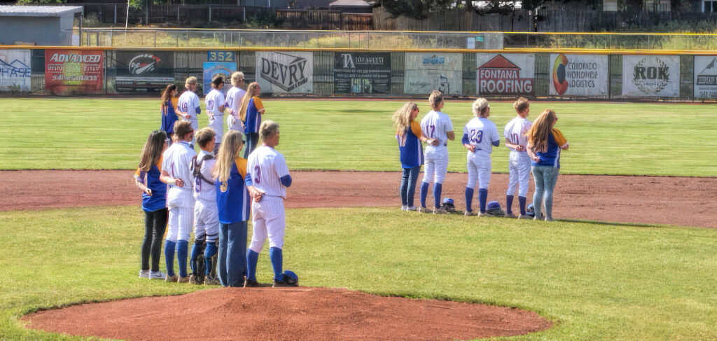 photo of several high school baseball and softball players standing on the field before a game.