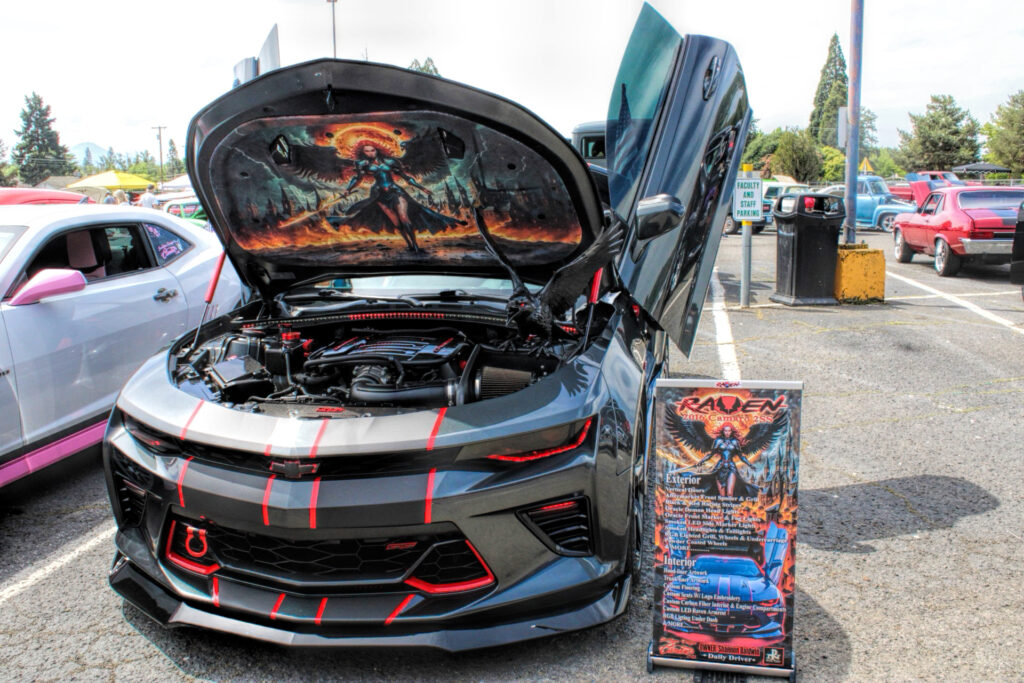 photo of a custom camero black with red accents and a mural of a winged female raven warrior on the underside of the hood.