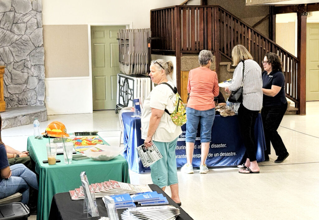 photo of three tables at an emergency management open house with agency representatives and citizens asking them questions.