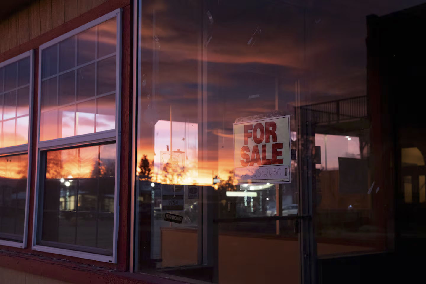 photo of the big glass window on a diner at sunset, the sunset reflects in the window and you can see a "for sale" sign.