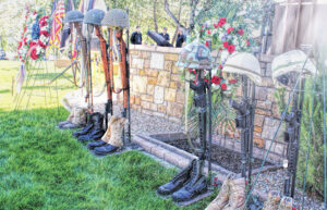 Photo of a row of empty boots with guns in them and helmets on top representing fallen soldiers from various US wars.