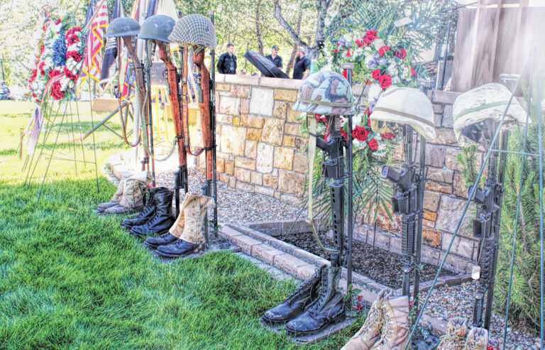 Photo of a row of empty boots with guns in them and helmets on top representing fallen soldiers from various US wars.