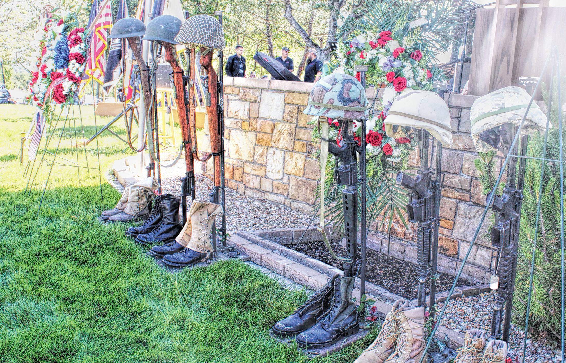 Photo of a row of empty boots with guns in them and helmets on top representing fallen soldiers from various US wars.
