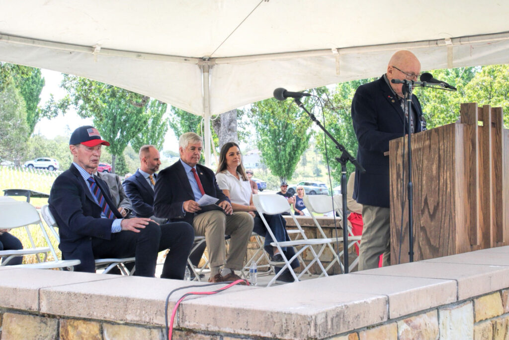 Photo of politicians and others sitting under a canopy as one individual speaks.