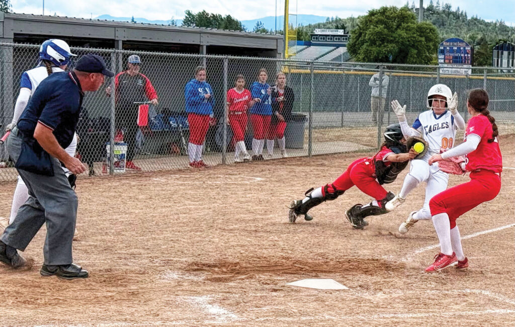 photo of a high school softball game with three players at home plate and the umpire looking on closely.
