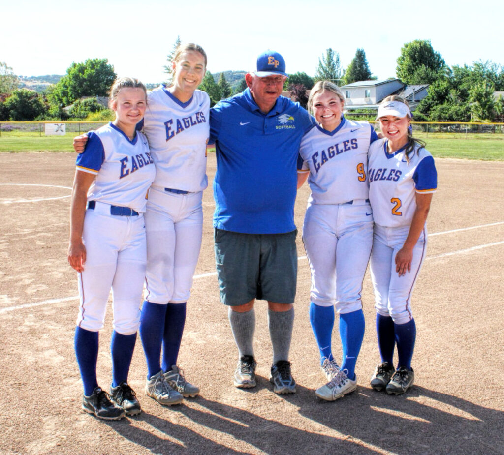 photo of four high school softball players and their coach in the middle.