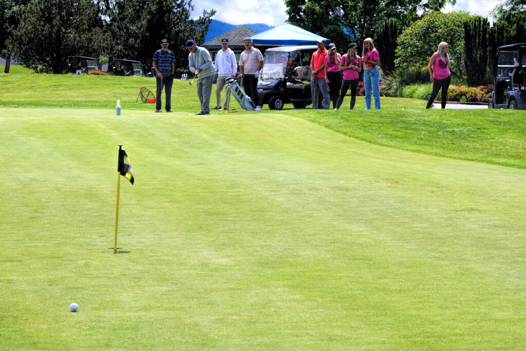 photo of several people watching a golfer who has just putted. The ball went past the hole.