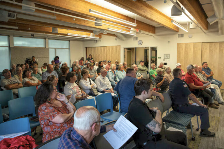 photo of a crowd of people seated in rows of chairs in a meeting hall.