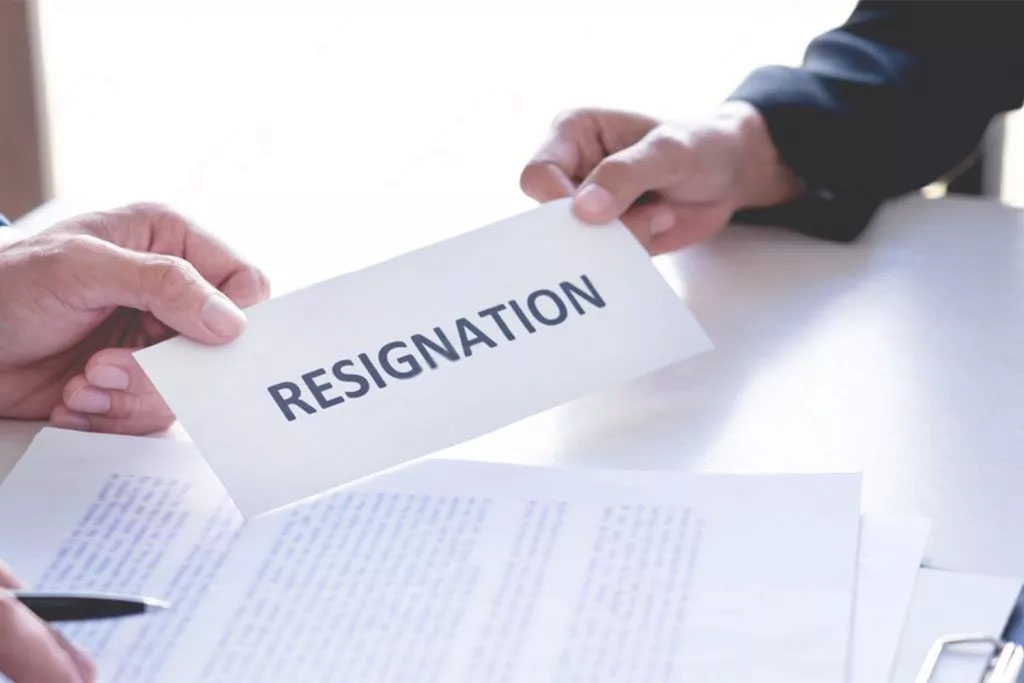 photo of two hands over a desk with one handing the other a card reading "resignation"
