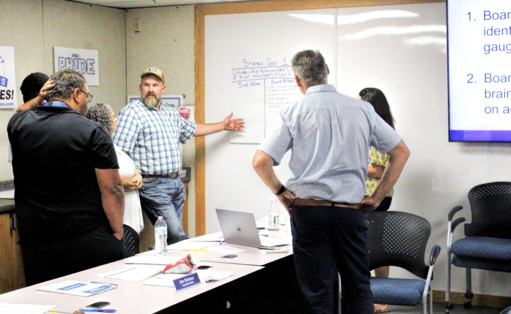 photo of a man gesturing toward a white board as other board members look on.