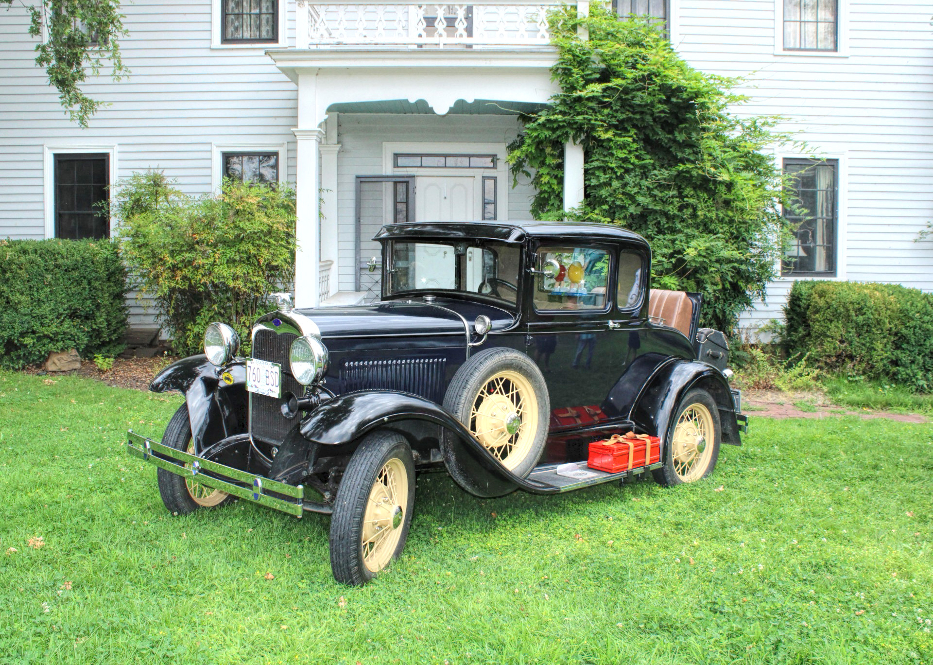 photo of a black vintage car with a rumble seat parked n front of a white old time mansion like house.