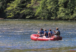 photo of four people in a red inflatable raft on the rogue river. all four are wearing life jackets.