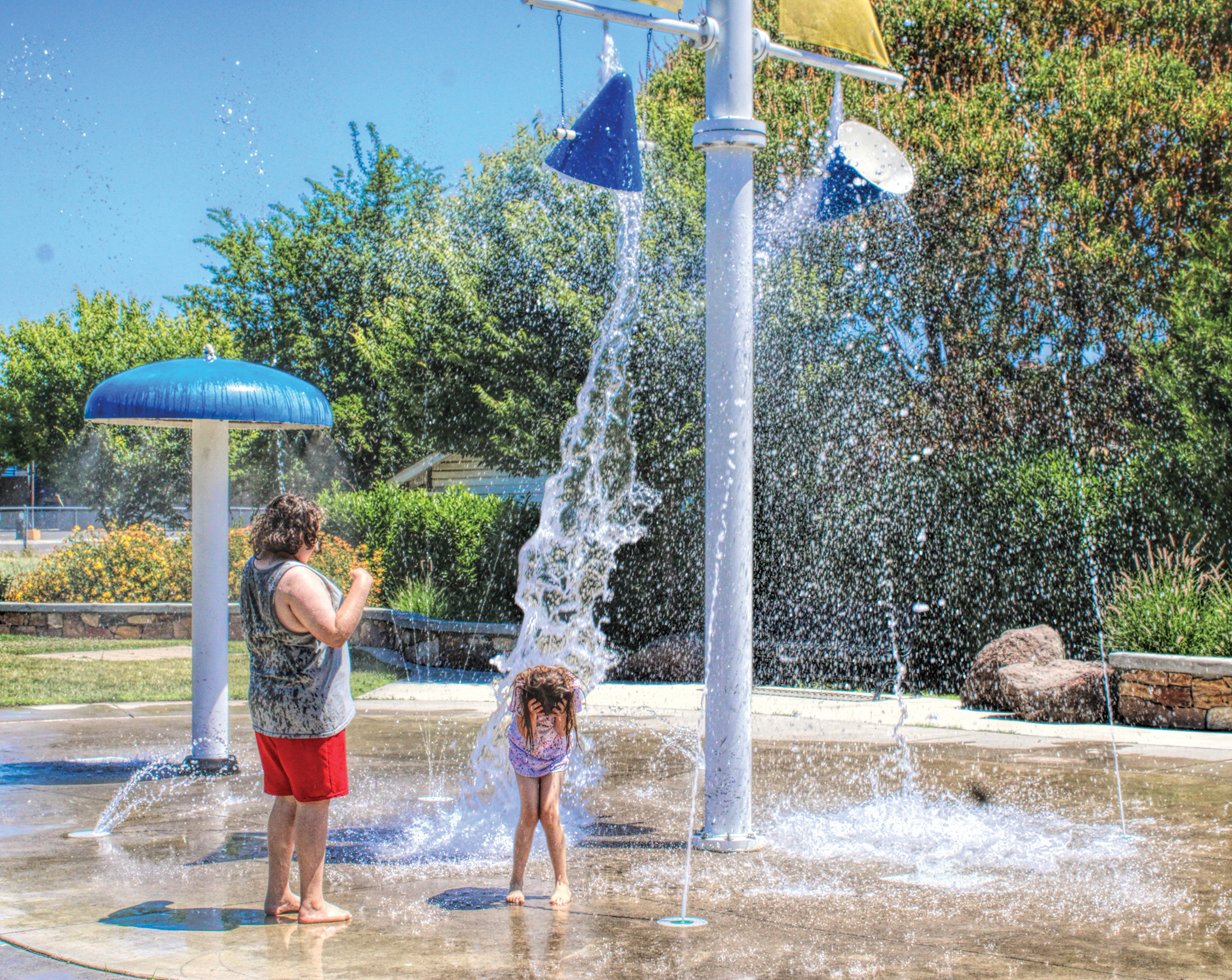 photo of one adult and one child at a small water park. a large bucket of water is splashing down on the child as sh ducks.