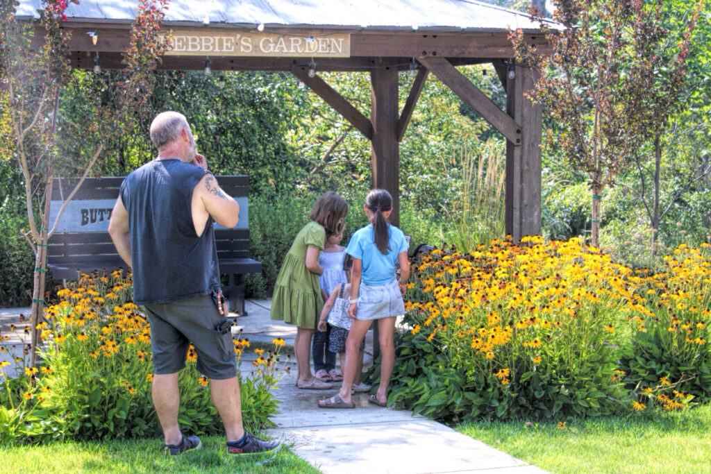photo of an adult male (father or grandfather) and three young girls looking at blooming black eyed susan flowers.