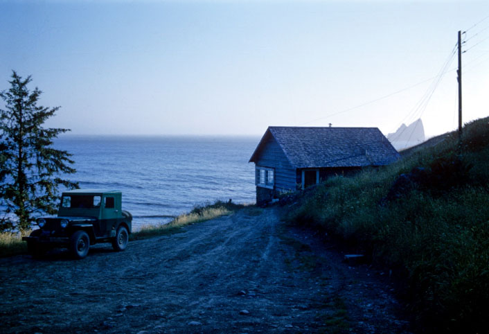 photo of a small cottage by the pacific ocean with an old jeep parked in front.
