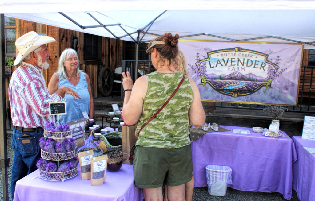 photo of two patrons talking to the vendors at a lavender farm table at a farmers market.