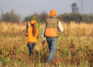 Photo of a tween girl and adult male wearing three mile orange clothing and walking in a field.