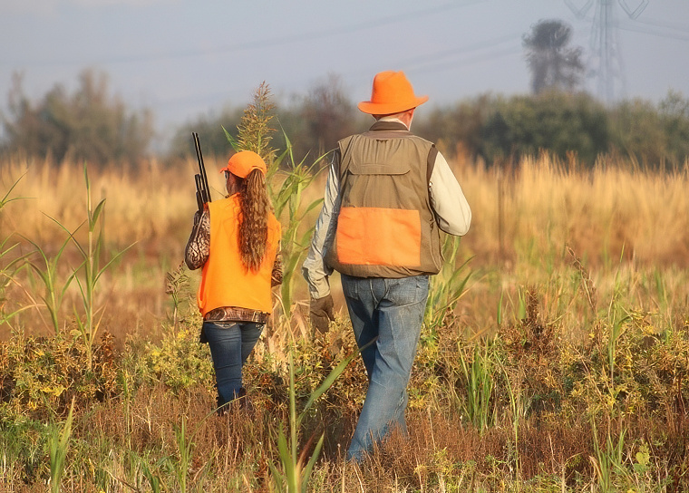 Photo of a tween girl and adult male wearing three mile orange clothing and walking in a field.