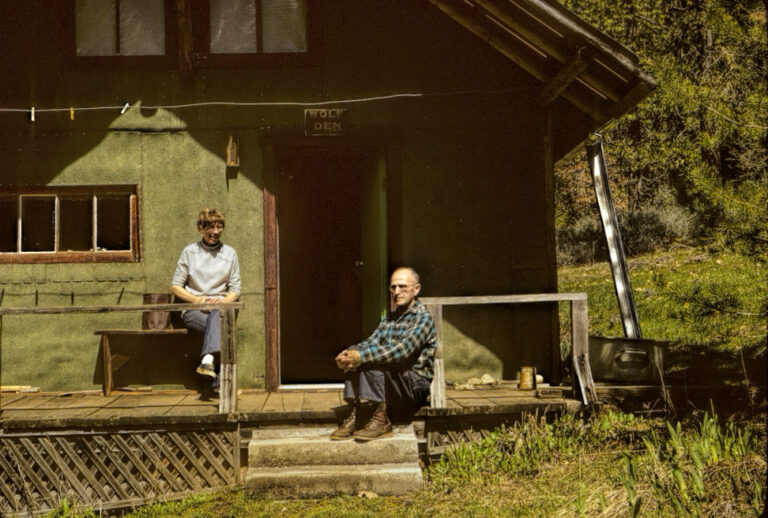 photo of a man and a woman sitting on the porch of a cabin.