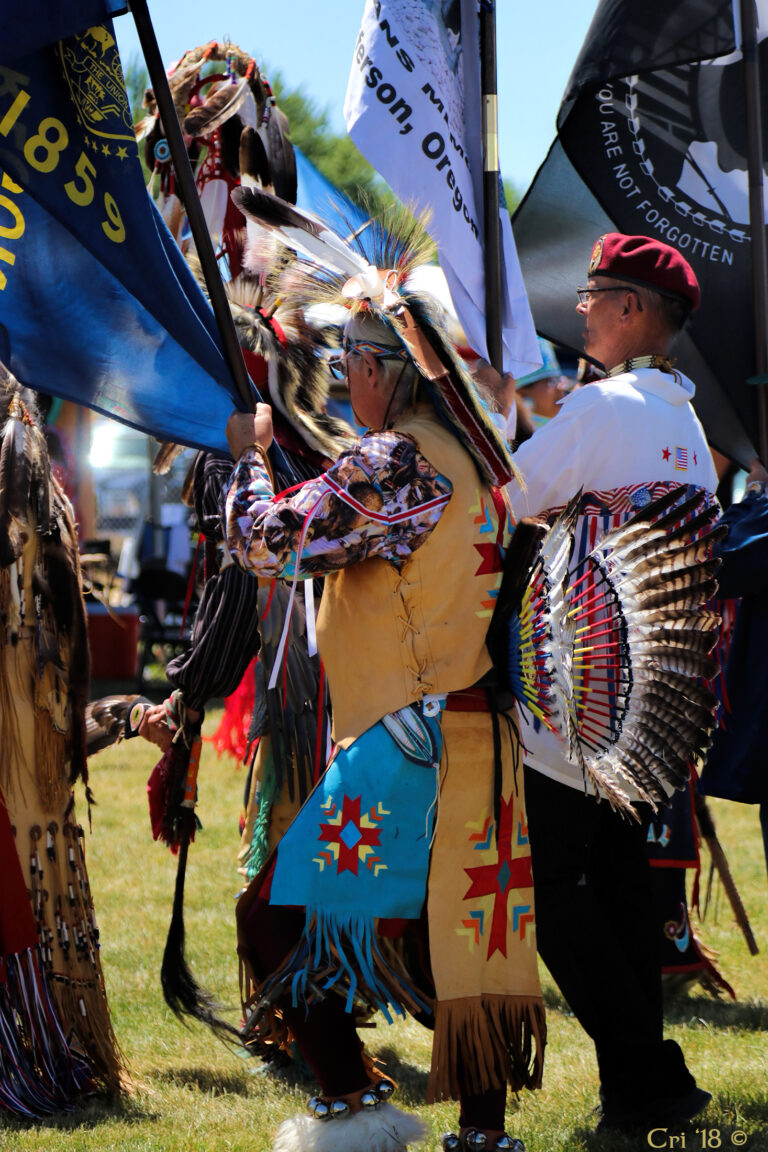 photo of Native American veteran honor guard in regalia holding various flags.