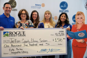photo of five people holding a giant check in the amount of $1,500 the memo reads :Dolly Parton Imagination Library. To their right is a life-sized cardboard Dolly