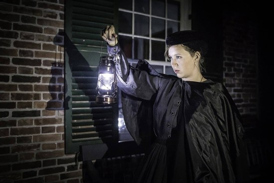 photo of a woman in victorian dress holding up a gas lantern.