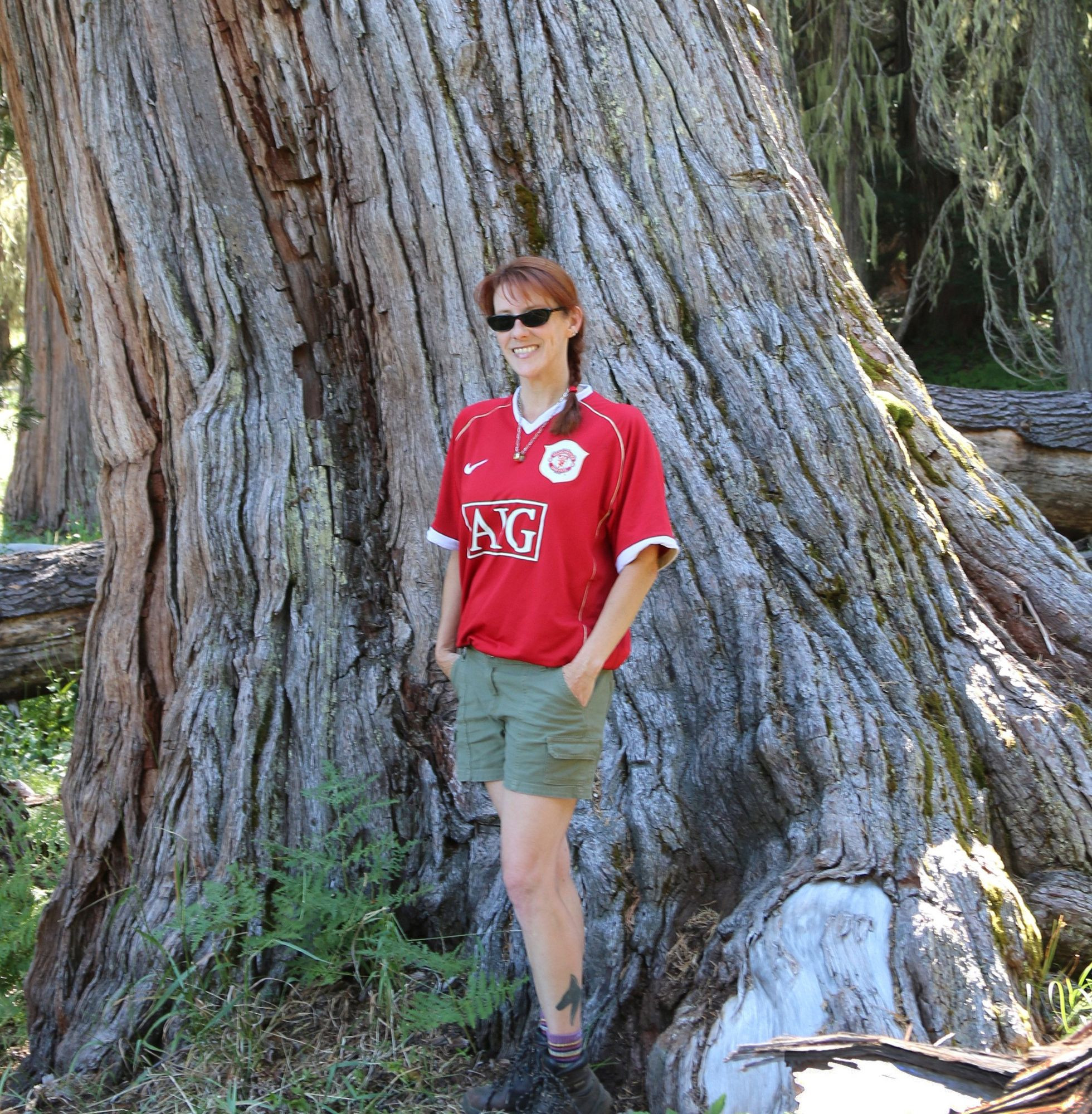 photo of a female in front of the enormous trunk of a red cedar.