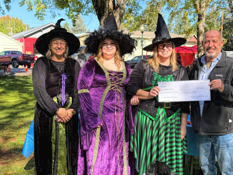 photo of three women dressed as witches and one man who is handing them an oversized check.