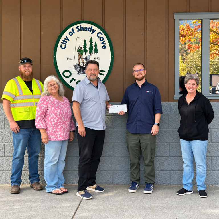 photo of four city employees and a pacific power employee. the pac power employee is handing one of the employees an oversized check.