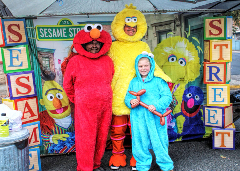 photo of two adults and one child dressed as sesame street characters Elmo, Big Bird and Cookie Monster. they are standing in a Sesame Street booth.