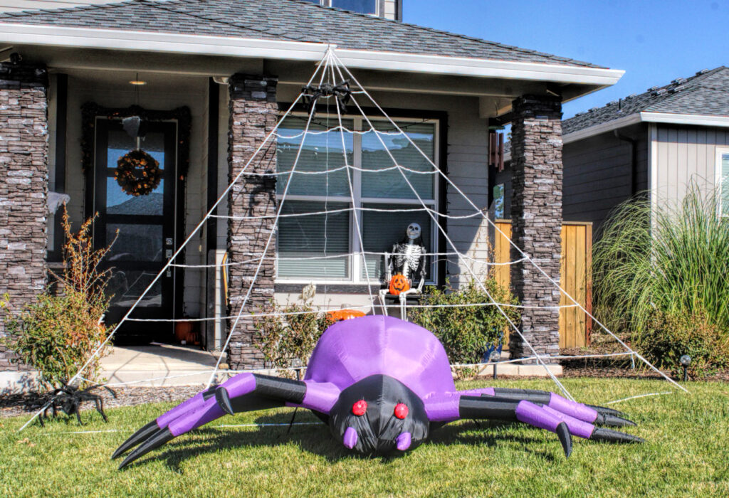 photo of a home decorated for halloween with a giant spider web and black and purple inflatable spider.
